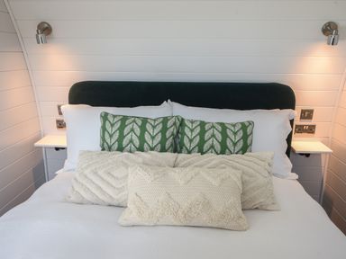 A bed with white bedding green and white patterned pillows and wall-mounted reading lights at Maple in Wootton Fitzpaine near Charmouth