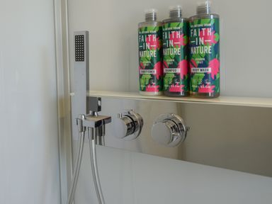 A shower area with a handheld showerhead and three bottles of Faith In Nature products at Maple in Wootton Fitzpaine near Charmouth