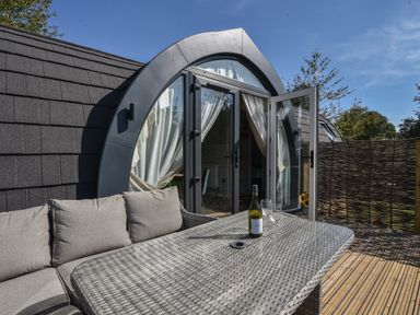 An outdoor patio with a wicker table and cushioned seating outside a curved glass door at Maple in Wootton Fitzpaine near Charmouth