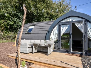 A curved cabin with glass doors and white curtains with outdoor patio furniture on a wooden deck at Maple in Wootton Fitzpaine near Charmouth