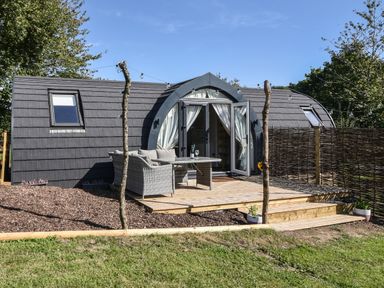 A small modern cabin with a curved roof and open double doors on a wooden deck with outdoor furniture at Maple in Wootton Fitzpaine near Charmouth