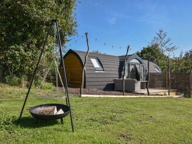 A small outdoor cabin with a curved roof and patio furniture near a hanging fire pit on grass at Maple in Wootton Fitzpaine near Charmouth