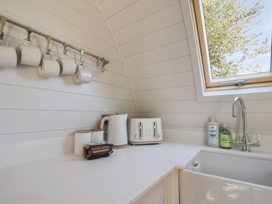 A kitchen corner with a kettle toaster mugs hanging on a rack and a sink under a window at Maple in Wootton Fitzpaine near Charmouth