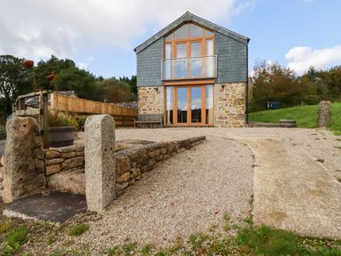 A two-story stone and wood house with glass balcony and gravel driveway at The Orchard in Cardinham
