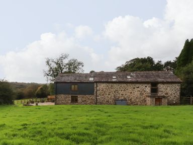 A stone barn conversion with grass field and trees surrounding at The Orchard in Cardinham