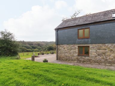 A stone and slate building next to grass and gravel area with trees in background at The Orchard in Cardinham
