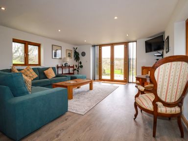 A living room with teal sofas a wooden coffee table and glass doors leading outside at The Orchard in Cardinham