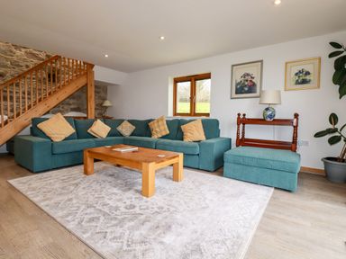 A living room with a teal sectional sofa and wooden coffee table near a wooden staircase at The Orchard in Cardinham