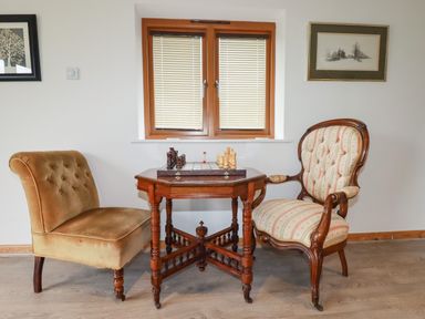 A room with two chairs and a wooden table with a chess set under a window at The Orchard in Cardinham