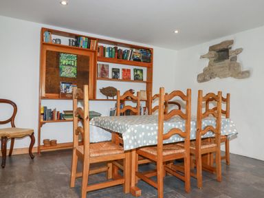 A dining room with a wooden table covered with a polka dot tablecloth and six wooden chairs at The Orchard in Cardinham