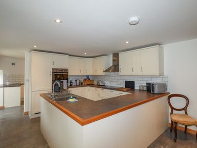 A kitchen with white cabinets a countertop a sink and a wooden chair at The Orchard in Cardinham