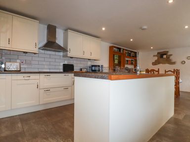 A kitchen with white cabinets a stove hood a toaster and a countertop island at The Orchard in Cardinham