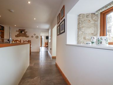 A hallway with tiled floor and white walls featuring framed pictures and window ledge pots at The Orchard in Cardinham