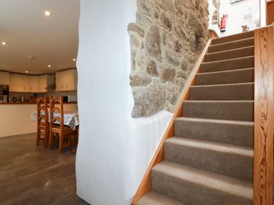 A carpeted staircase next to a stone wall and a kitchen with a dining table and chairs at The Orchard in Cardinham