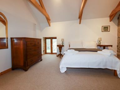 A bedroom with a bed folded towels wooden chest of drawers and exposed wooden beams at The Orchard in Cardinham