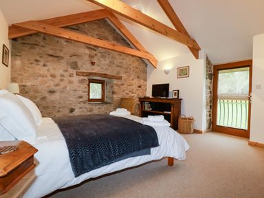 A bedroom with a bed a television on a wooden stand and a door with a window at The Orchard in Cardinham