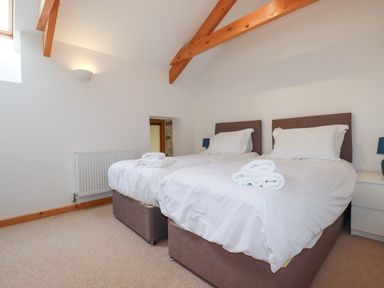 A bedroom with two single beds white bedding folded towels and wooden beams on the ceiling at The Orchard in Cardinham