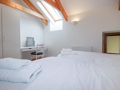 A bedroom with two beds with white sheets and towels a desk with a chair a mirror skylight windows and wooden beams at The Orchard in Cardinham