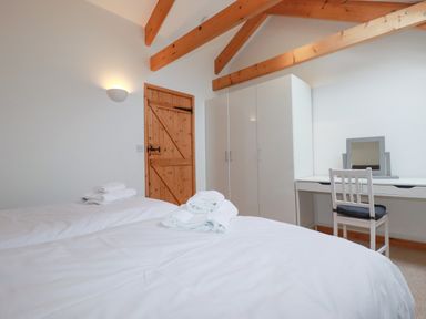 A bedroom with two single beds with towels on them a wooden door a white wardrobe and a desk with a chair and mirror at The Orchard in Cardinham