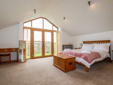 A bedroom with a wooden bed and chest in front of large glass doors with a view at The Orchard in Cardinham