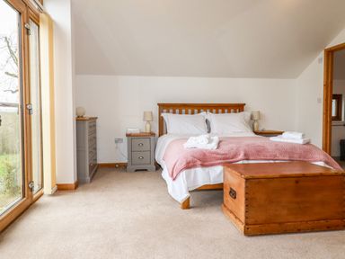 A bedroom with a double bed bedside tables a chest and large windows at The Orchard in Cardinham
