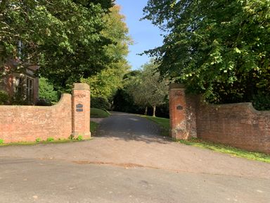 A driveway entrance with brick pillars and walls surrounded by trees at The Hideaway in Uplyme near Lyme Regis