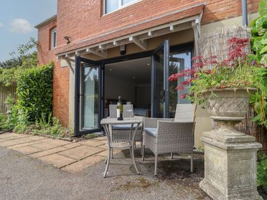 An outdoor patio with table and chairs next to open glass doors and a large planter at The Hideaway in Uplyme near Lyme Regis