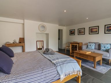 A bedroom with a bed sofa coffee table dining table and framed pictures on the wall at The Hideaway in Uplyme near Lyme Regis