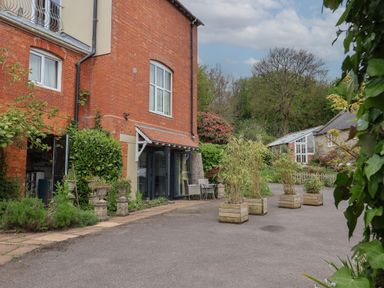 A brick building with potted plants and outdoor seating next to a paved area at The Hideaway in Uplyme near Lyme Regis