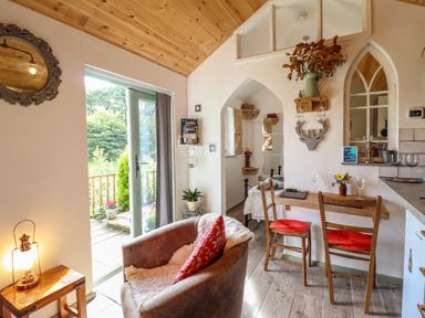 A small living area with a leather armchair a wooden table with two chairs and a view of a bedroom at Chateau Petit in Trefeglwys