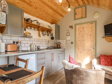 A kitchen area with gray cabinets wooden ceiling and beige walls next to a dining table and armchairs at Chateau Petit in Trefeglwys