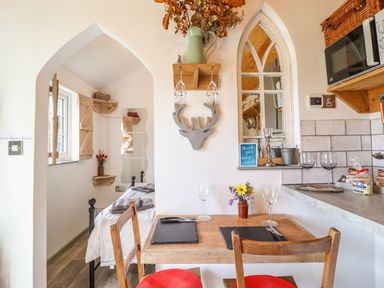A dining table with two chairs and place settings in a small kitchen area with an arched doorway leading to a bedroom at Chateau Petit in Trefeglwys