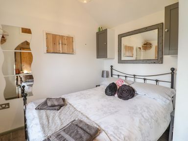 A bedroom with a metal bed frame a patterned bedspread and pillows two wall cabinets a large mirror and a wavy wall mirror at Chateau Petit in Trefeglwys