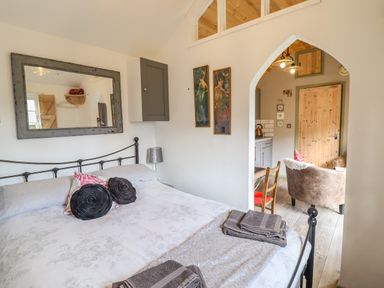 A bedroom with a bed and pillows a mirror on the wall and an archway leading to a living area at Chateau Petit in Trefeglwys