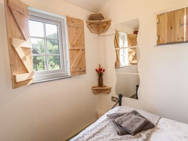 A bedroom with a bed folded towels a window with wooden shutters a wall mirror and wooden corner shelves at Chateau Petit in Trefeglwys