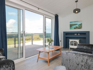 A living room with glass sliding doors a wooden coffee table and a small fireplace at Buttercup Lodge in Norton near Dartmouth