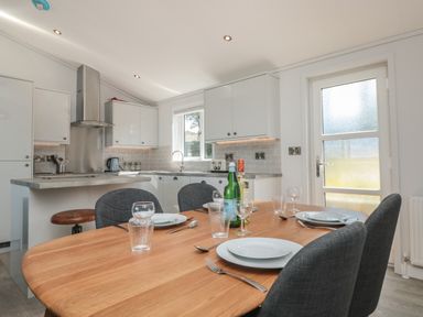 A kitchen with white cabinets a wooden dining table set for four and a door with frosted glass at Buttercup Lodge in Norton near Dartmouth