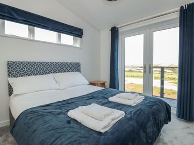 A bedroom with a double bed blue blanket white towels bedside table and glass doors at Buttercup Lodge in Norton near Dartmouth