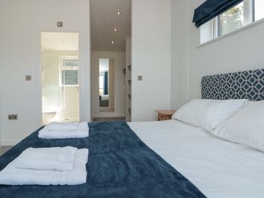 A bedroom with a bed covered with white linens and a blue blanket with towels on it and an adjoining bathroom with a shower at Buttercup Lodge in Norton near Dartmouth