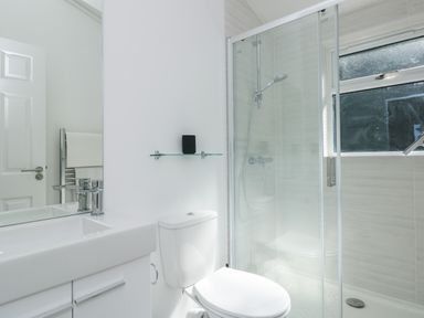 A bathroom with a white sink vanity, a toilet, a glass shower enclosure, and a towel rack with white towels at Buttercup Lodge in Norton near Dartmouth