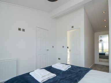 A bedroom with a bed covered by blue blanket and white towels on top two doors on the wall a mirror on another wall and a radiator at Buttercup Lodge Norton near Dartmouth