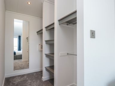 A walk-in closet with shelves hanging rods a mirror and carpet flooring at Buttercup Lodge in Norton near Dartmouth