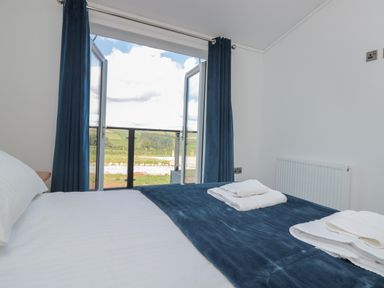 A bedroom with a bed covered in white and blue bedding and open doors leading outside at Buttercup Lodge in Norton near Dartmouth