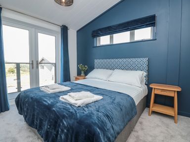 A bedroom with a double bed a blue blanket white towels and two wooden bedside tables at Buttercup Lodge in Norton near Dartmouth