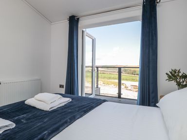 A bedroom with a bed white sheets and blue blanket open door leading to a balcony overlooking fields at Buttercup Lodge in Norton near Dartmouth