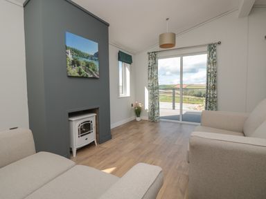 A living room with two beige sofas a small white stove and sliding glass doors with curtains at Honeysuckle Lodge in Norton near Dartmouth