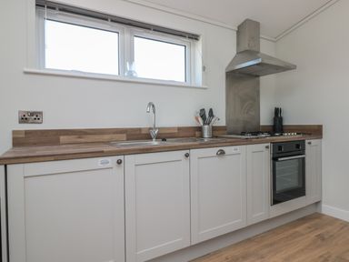A kitchen with white cabinets a wooden countertop a sink a stove and kitchen utensils at Honeysuckle Lodge in Norton near Dartmouth