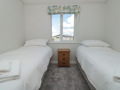 A bedroom with two single beds separated by a wooden nightstand under a window at Honeysuckle Lodge in Norton near Dartmouth