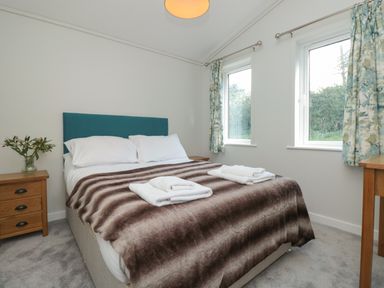 A bedroom with a double bed two windows and a bedside table with flowers at Honeysuckle Lodge Norton near Dartmouth