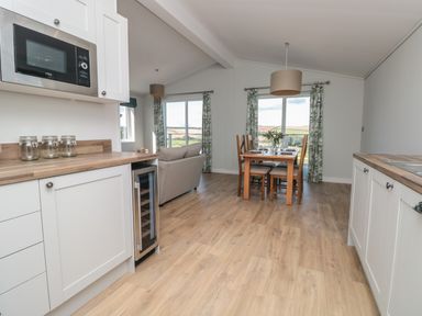 A kitchen and dining area with white cabinets wooden countertops a wine cooler a dining table with chairs and floral curtains at Primrose Lodge in Norton near Dartmouth